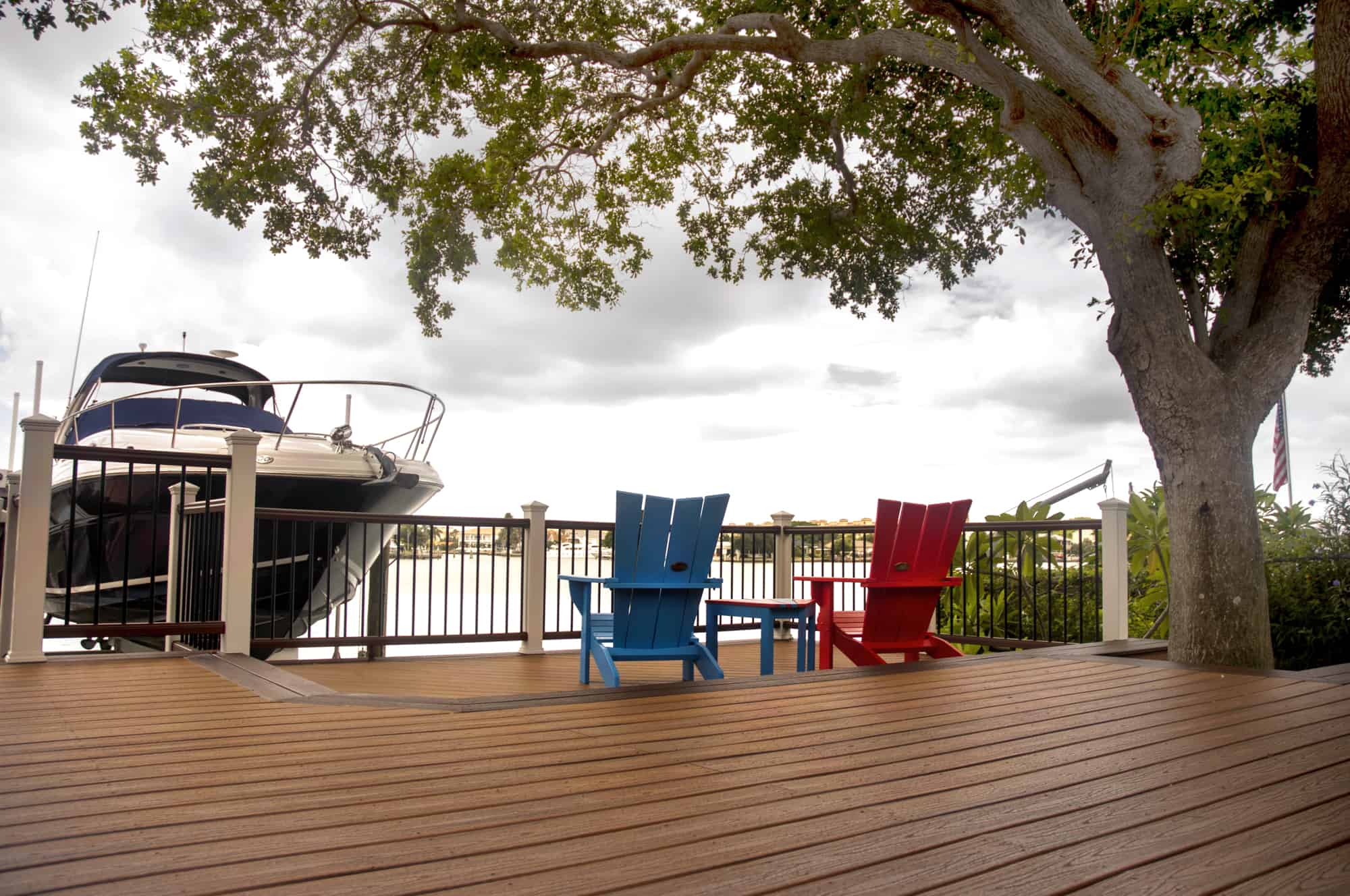 A deck on the water's edge installed with premium wood. There is a boat and two deck chairs.