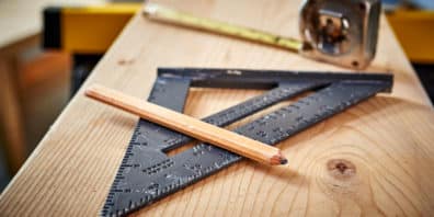 Woodworking tools sitting on a plank of wood. Includes pencil, measuring tape, and triangle ruler.